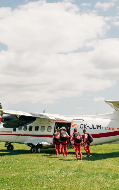 Paracaidistas con monos rojos suben al avión blanco OK-JUM estacionado sobre la hierba