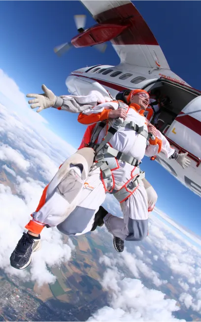 Instructor tándem y pasajero con monos blancos y naranjas abandonan la puerta del avión muy por encima de las nubes