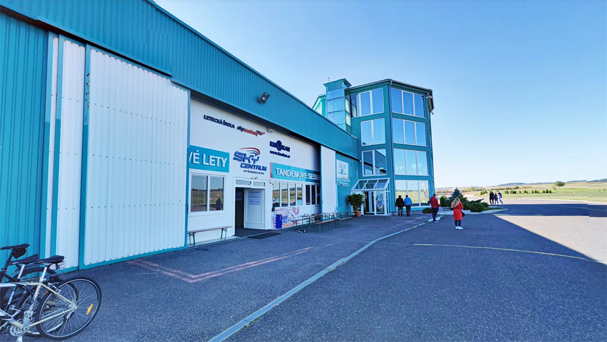 Hangar verde azulado y torre acristalada del aeródromo de Příbram con los rótulos Sky Centrum y Tandemové seskoky, bicis delante