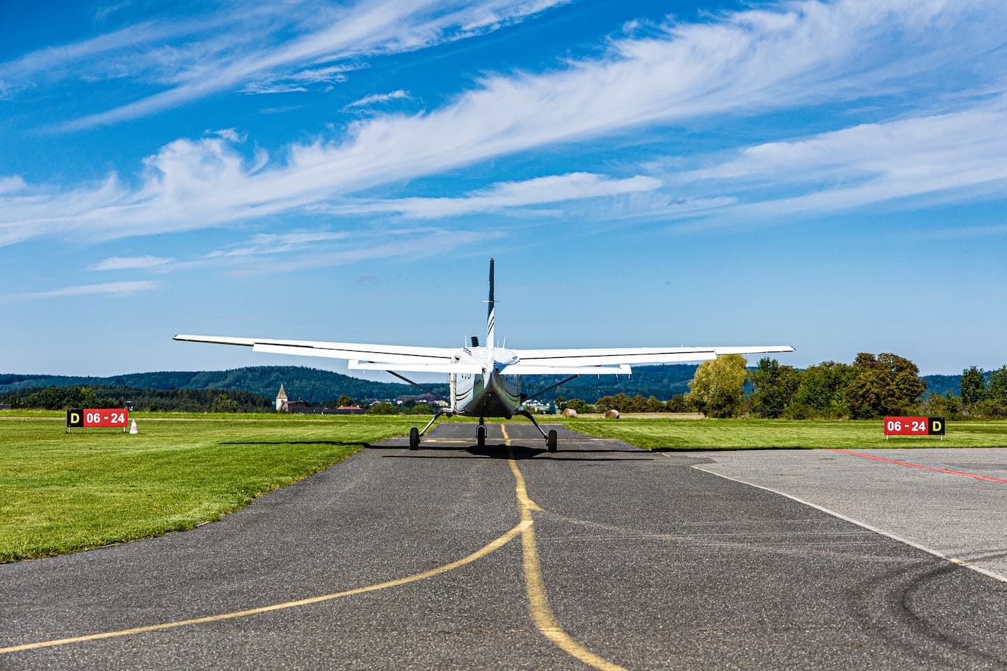 Příbram airport: single-engine high-wing aircraft seen from behind on the taxiway, runway 06-24 signs on the grass
