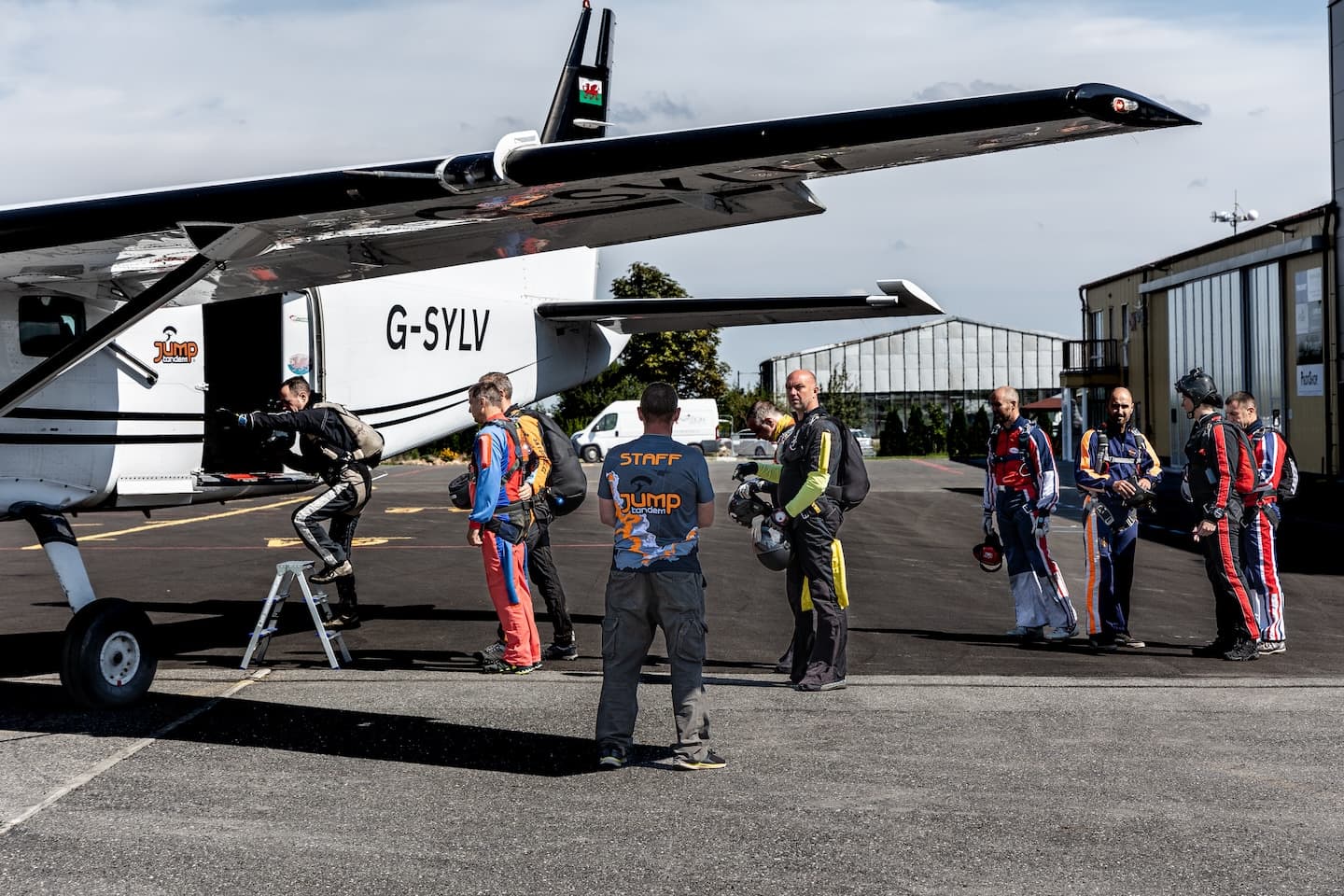 Aeródromo de Příbram: paracaidistas suben al avión blanco G-SYLV por una escalerilla; observa un empleado con camiseta de JUMP-TANDEM