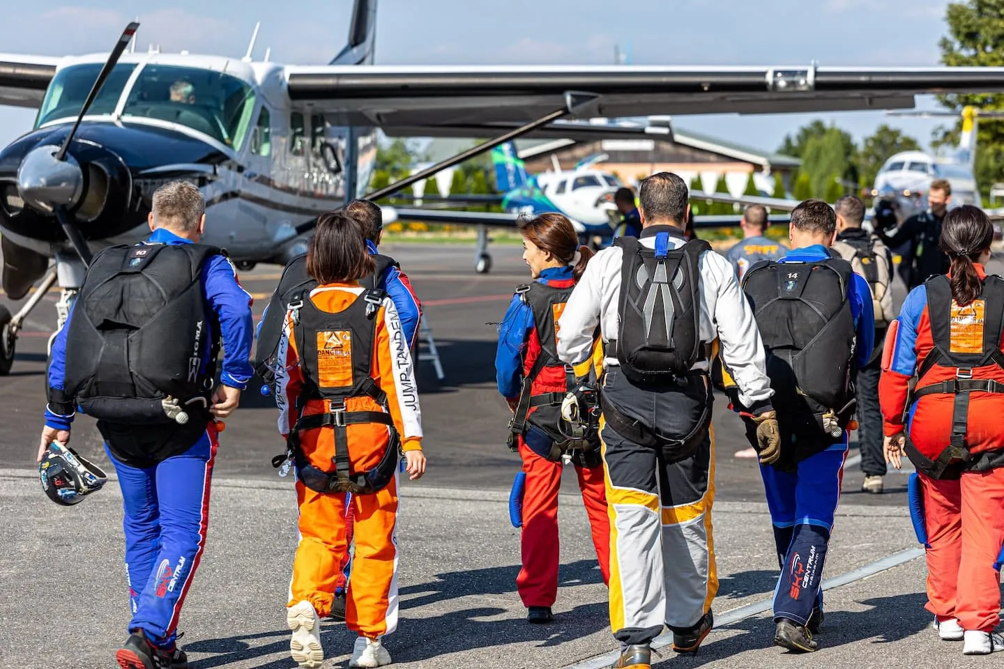 Příbram airport: tandem instructors and passengers in jumpsuits walking across the apron to the aircraft, seen from behind