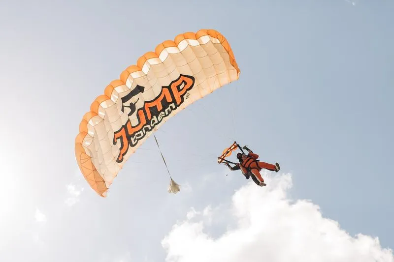 Tandem canopy with the JUMP-TANDEM logo in the sky above a white cloud, tandem instructor and passenger beneath it