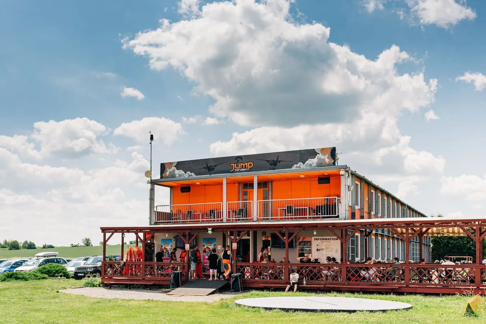Prostějov airport: orange JUMP-TANDEM building with a terrace and veranda, a car park on the left and a circular pad in the grass