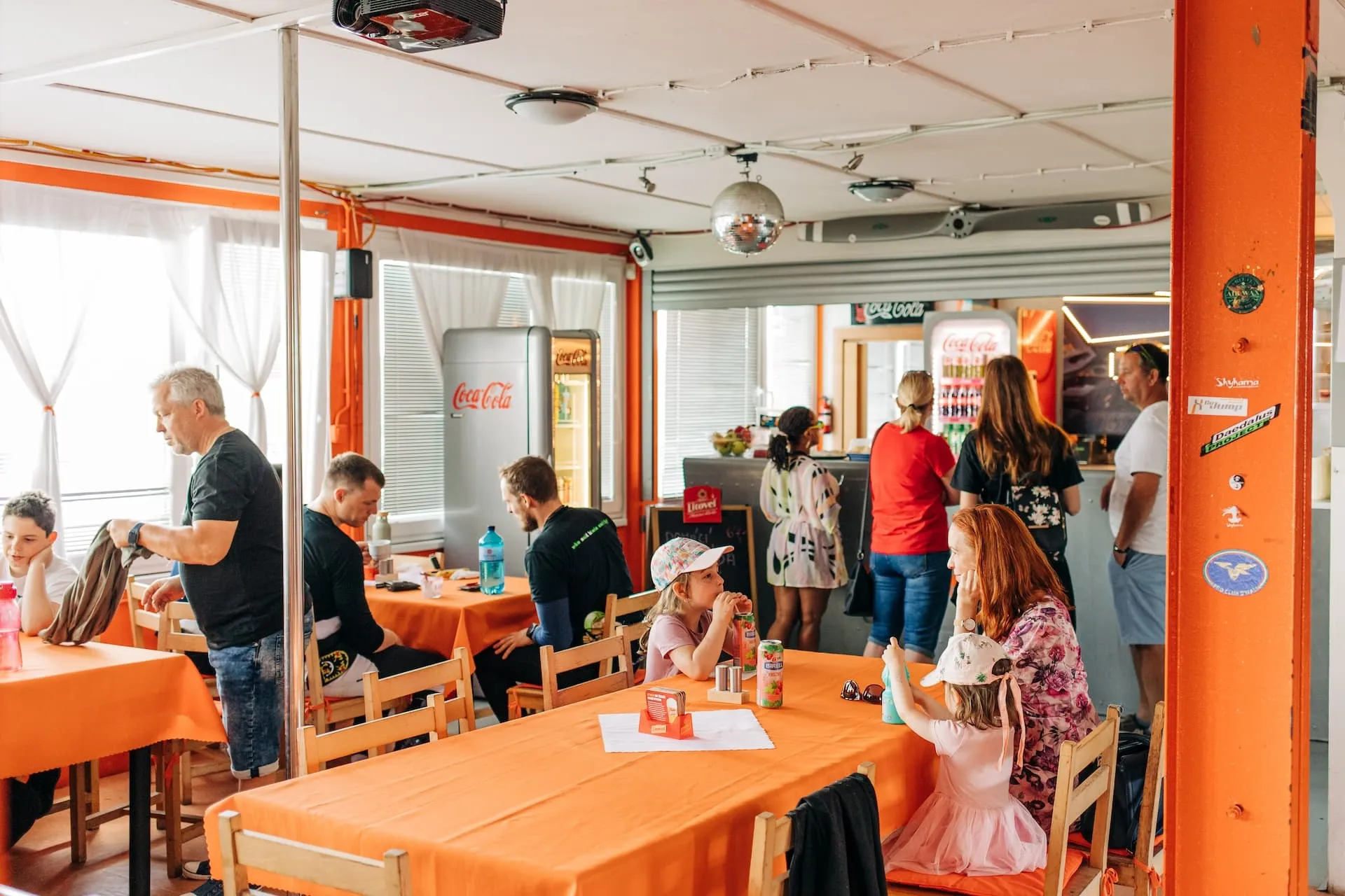 Prostějov airport: dining room with orange tablecloths, guests at the tables and at the bar with a Coca-Cola fridge