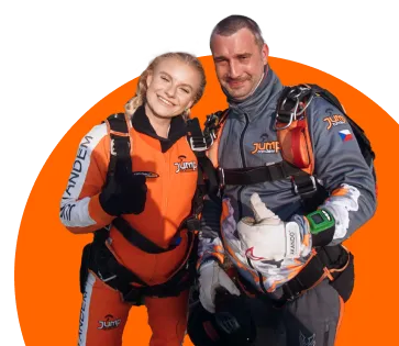 Una pasajera con mono naranja de JUMP-TANDEM y un instructor tándem de gris con el pulgar en alto, ante un círculo naranja