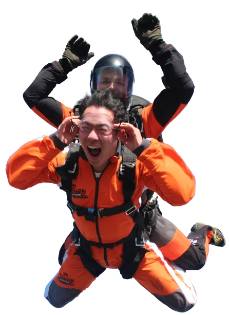 Passenger in an orange jumpsuit shouting with joy and holding his goggles, tandem instructor behind him with arms raised