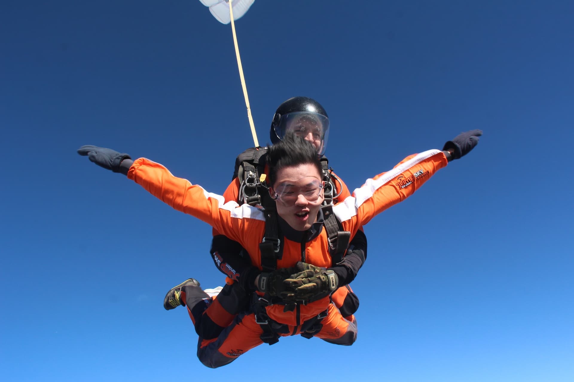 Caída libre en un cielo despejado: pasajero con mono naranja, brazos abiertos y boca abierta, con el paracaídas estabilizador encima
