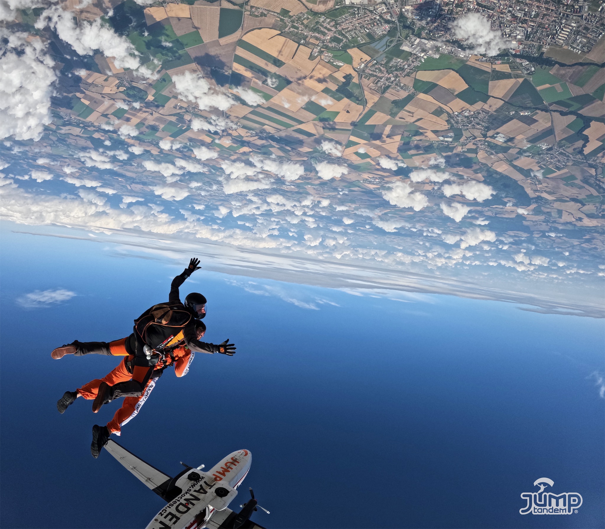Instructor tándem y pasajero en caída libre recién salidos del avión JUMP-TANDEM, en una toma invertida con campos y nubes arriba