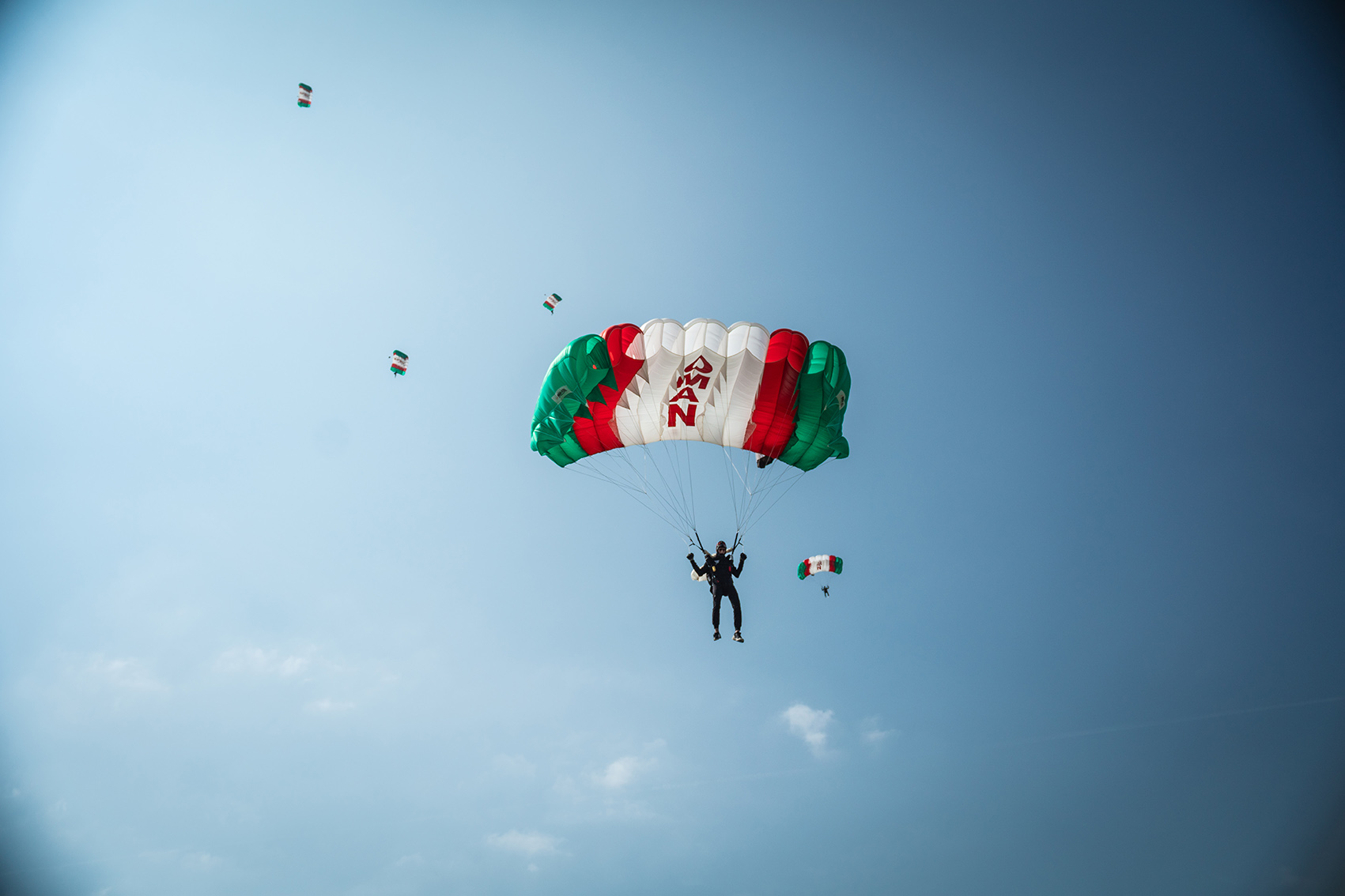 Campeonatos del Mundo FAI 2024: paracaidista bajo un paracaídas verde, blanco y rojo con la inscripción OMAN y más paracaídas al fondo