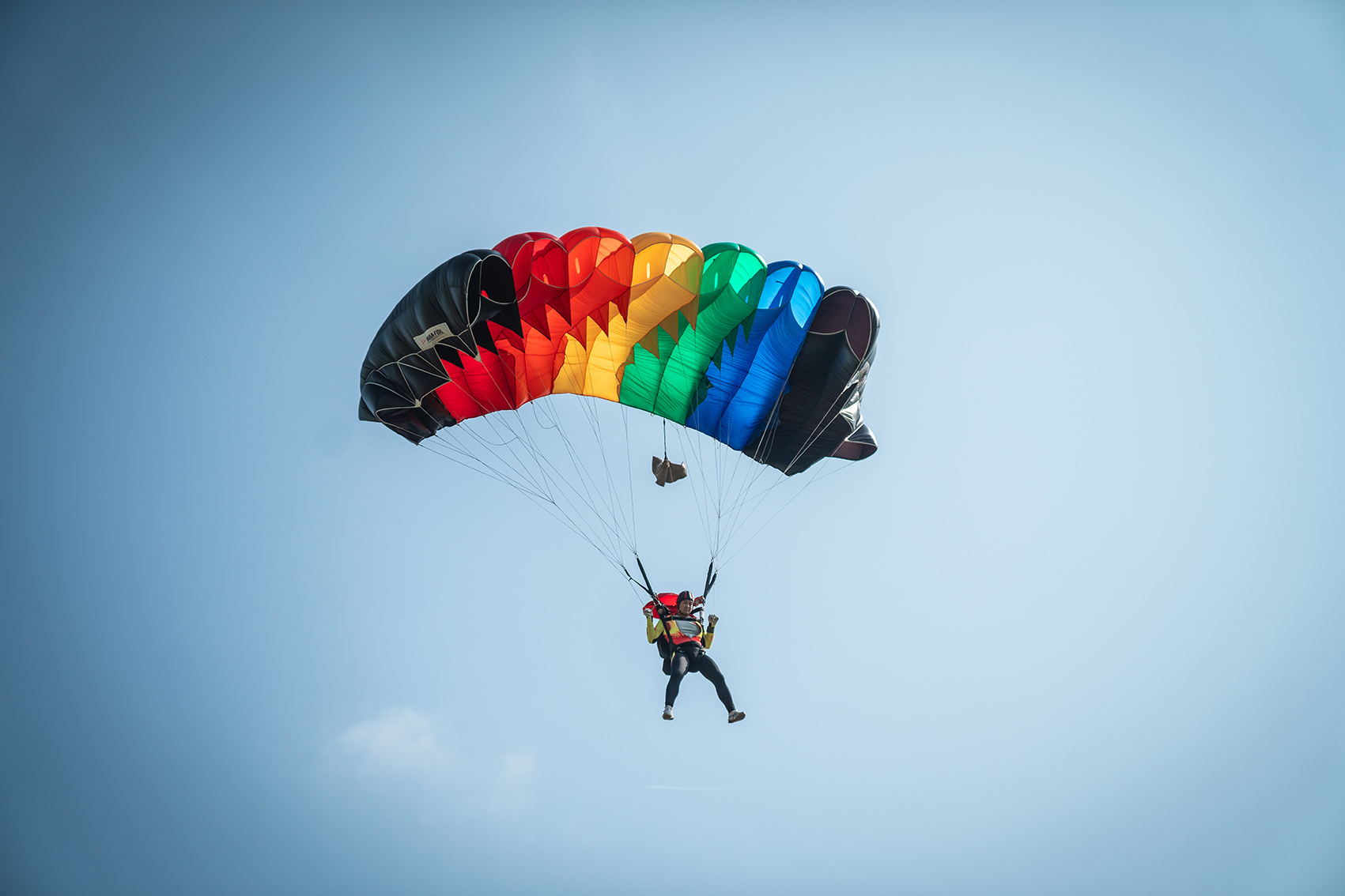Campeonatos del Mundo FAI 2024: paracaidista bajo un paracaídas con franjas arcoíris y bordes negros en un cielo azul despejado