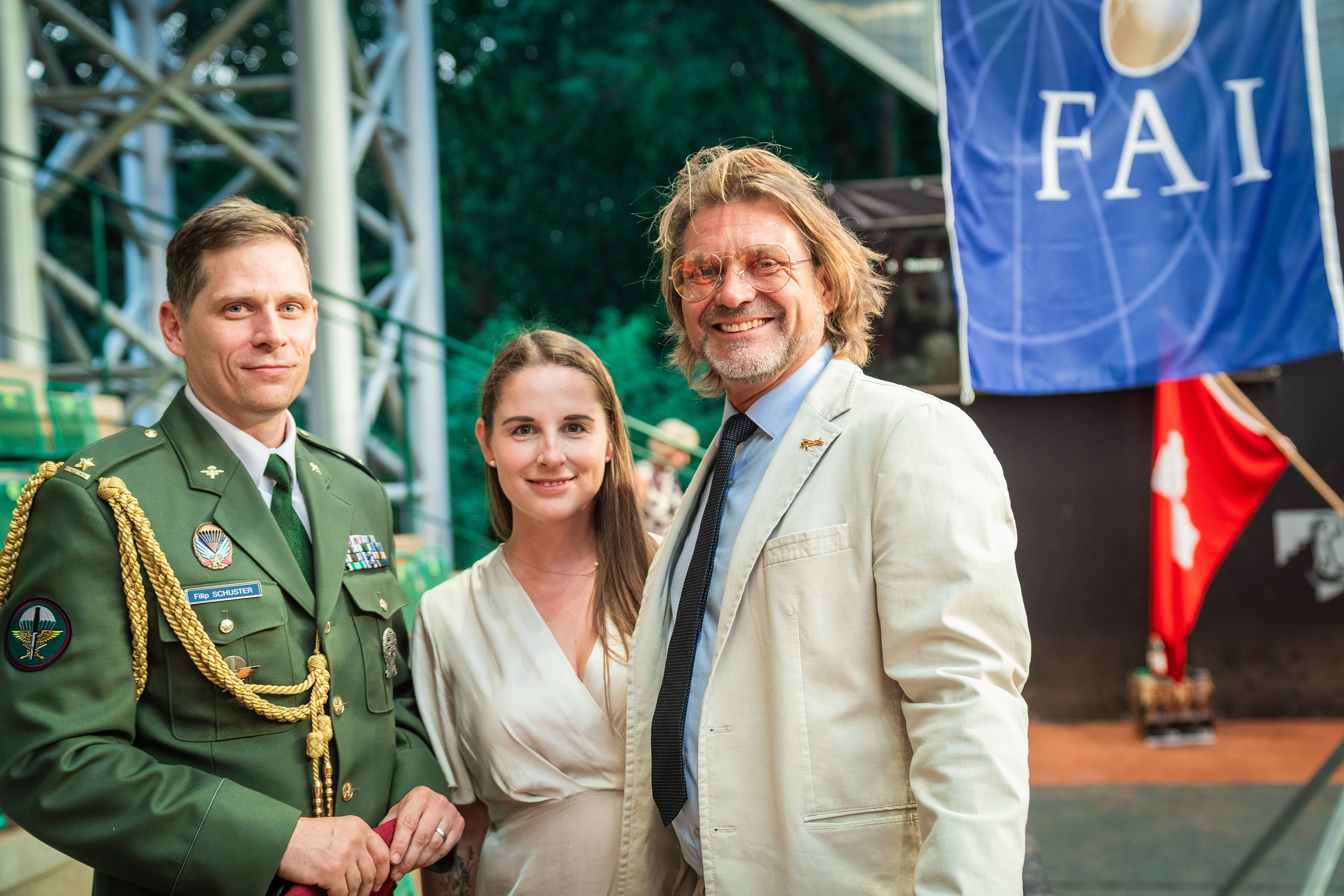 Campeonatos del Mundo FAI 2024: un oficial con uniforme verde de gala, una mujer de crema y un hombre con traje claro bajo la bandera FAI