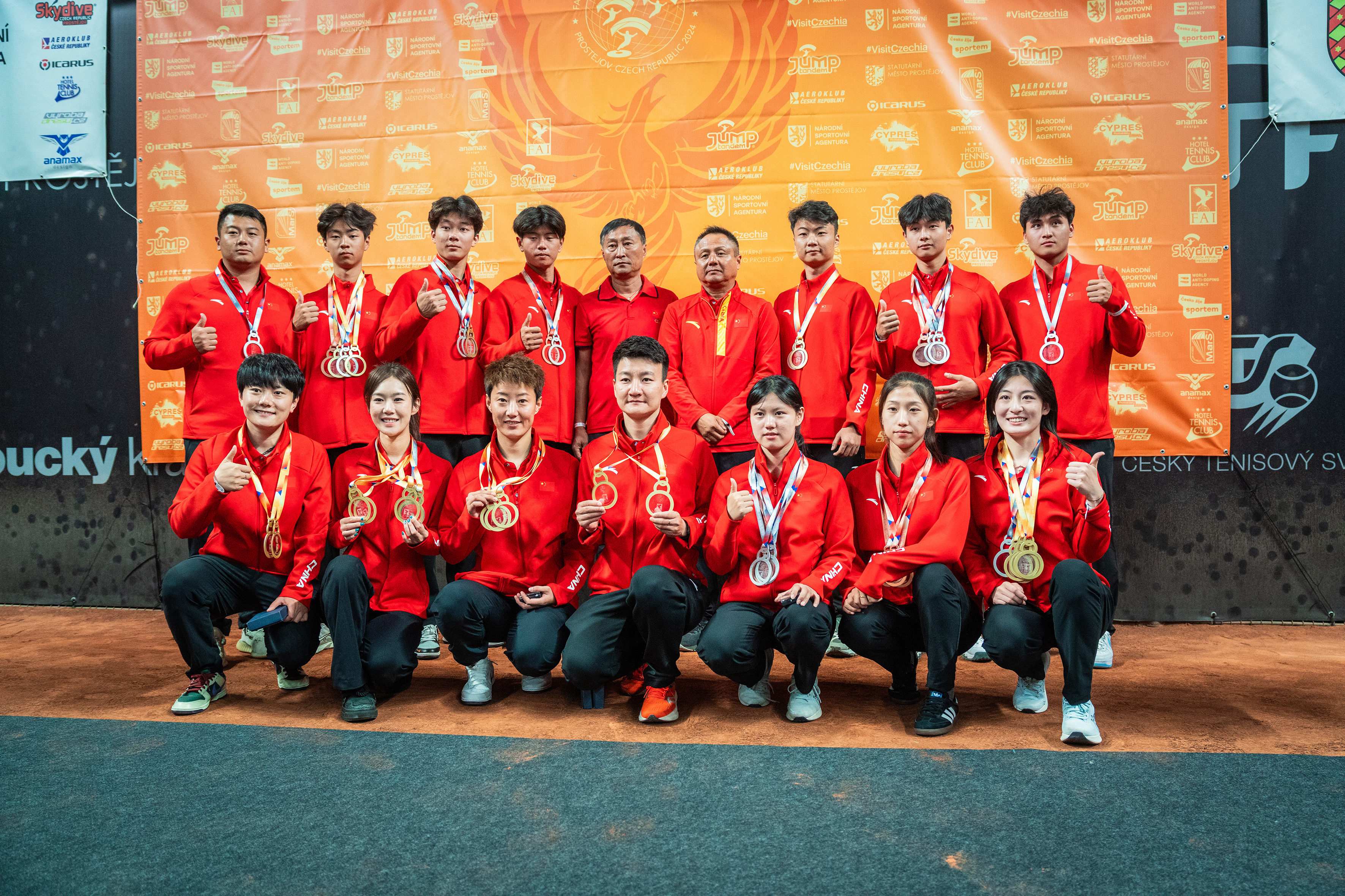 Campeonatos del Mundo FAI 2024: el equipo de China, de rojo, muestra sus medallas en dos filas ante el panel naranja de patrocinadores