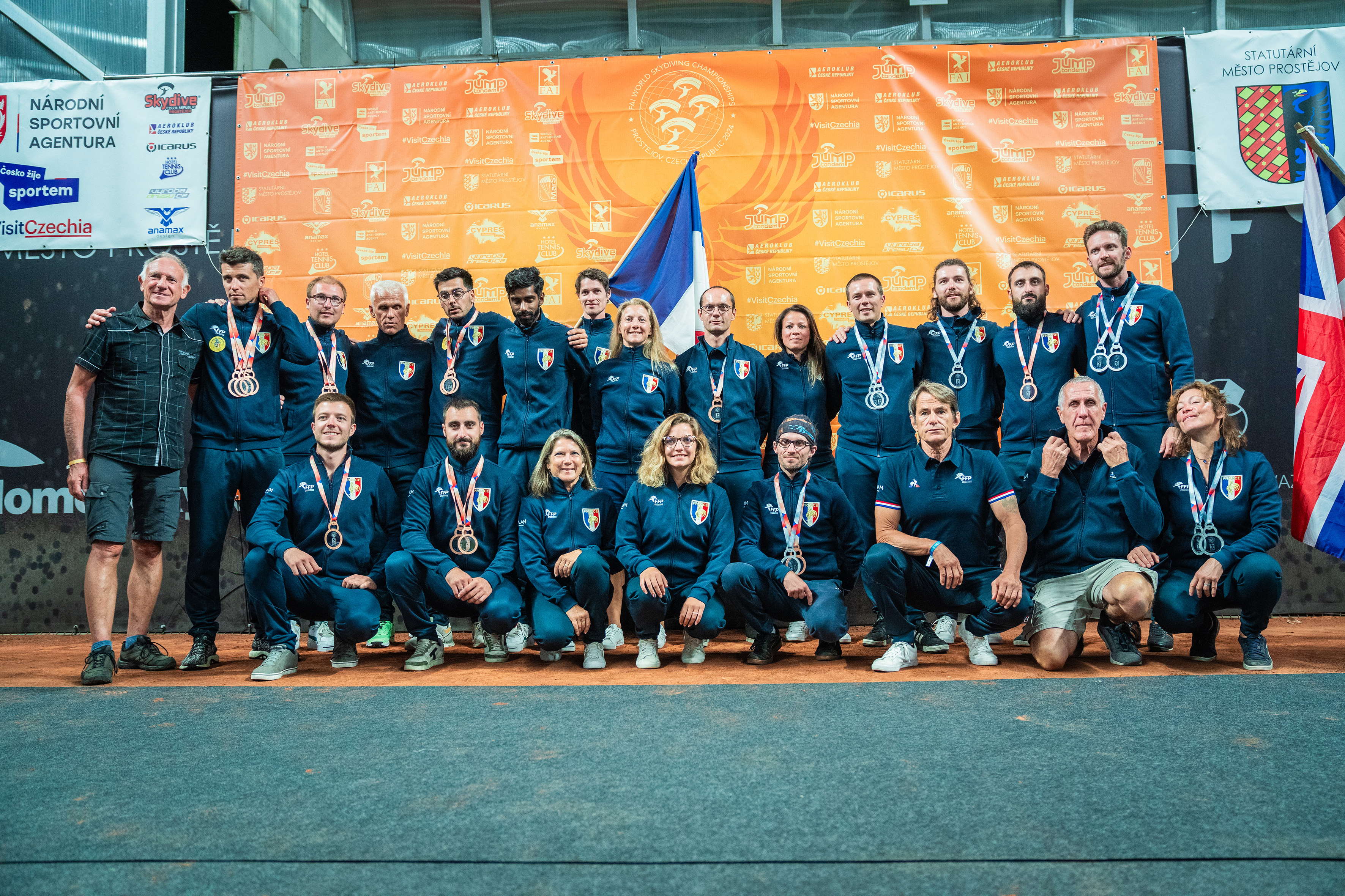 Campeonatos del Mundo FAI 2024: equipo con chándales azul marino, medallas y la bandera de Francia ante el panel naranja de patrocinadores
