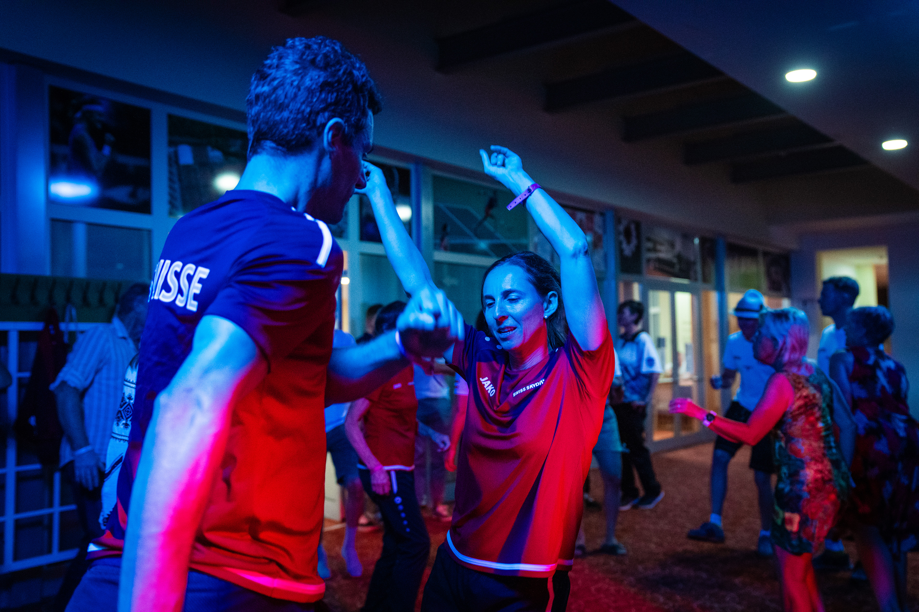 Campeonatos del Mundo FAI 2024: competidores con camisetas de equipo bailan en la fiesta nocturna bajo luces rojas y azules