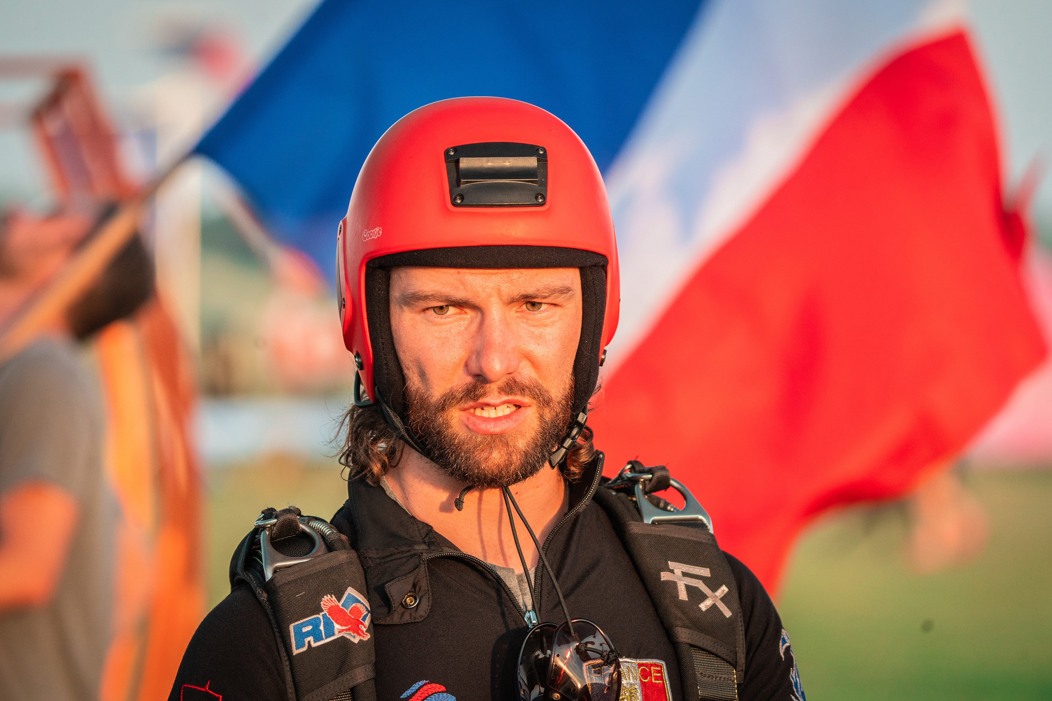 Campeonatos del Mundo FAI 2024: retrato de un paracaidista con casco rojo y arnés negro ante la bandera de Francia