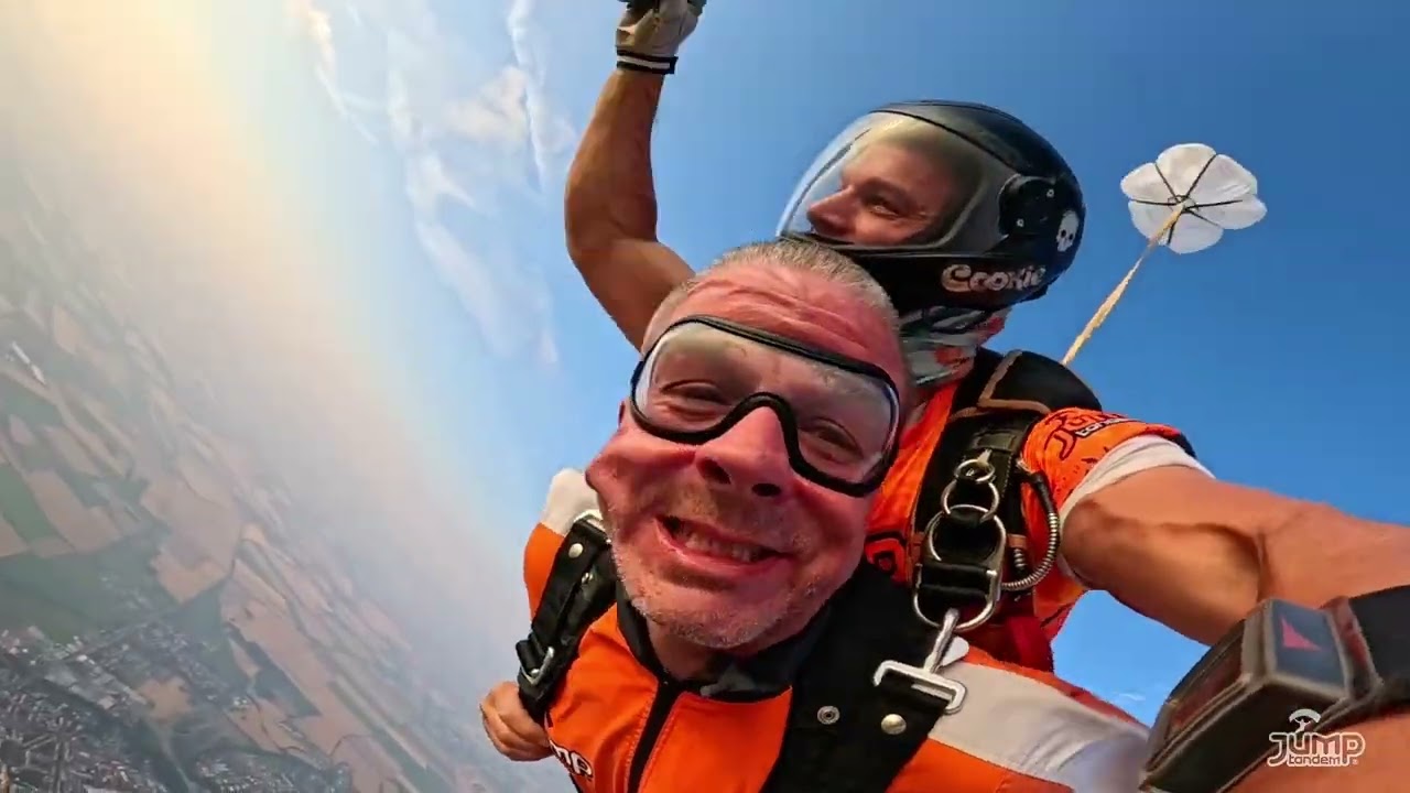 Play video: Handy camera (smiling passenger in goggles and tandem instructor in a black helmet in freefall)